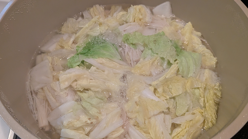 鶏団子のアクを取り、白菜とえのきを加えて煮込む様子